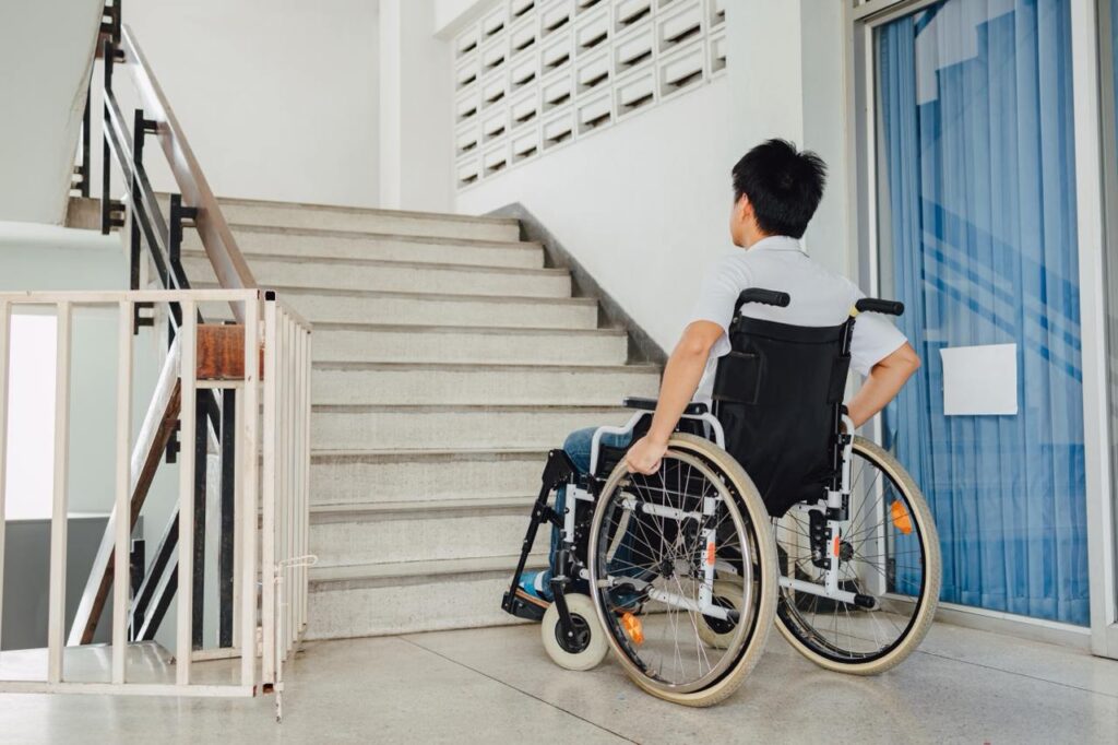 Man in wheelchair looking at a set of stairs inside a home